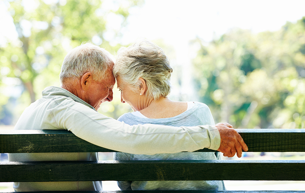 Elderly couple sitting outside on a bench.