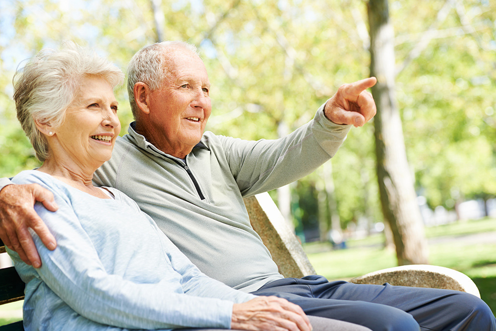 Elderly couple sitting outside on a bench together.