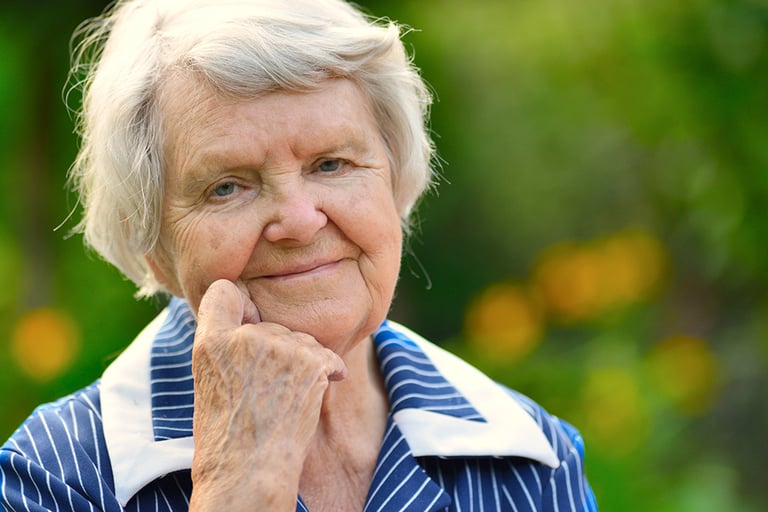 Elderly woman sitting outside and smiling.