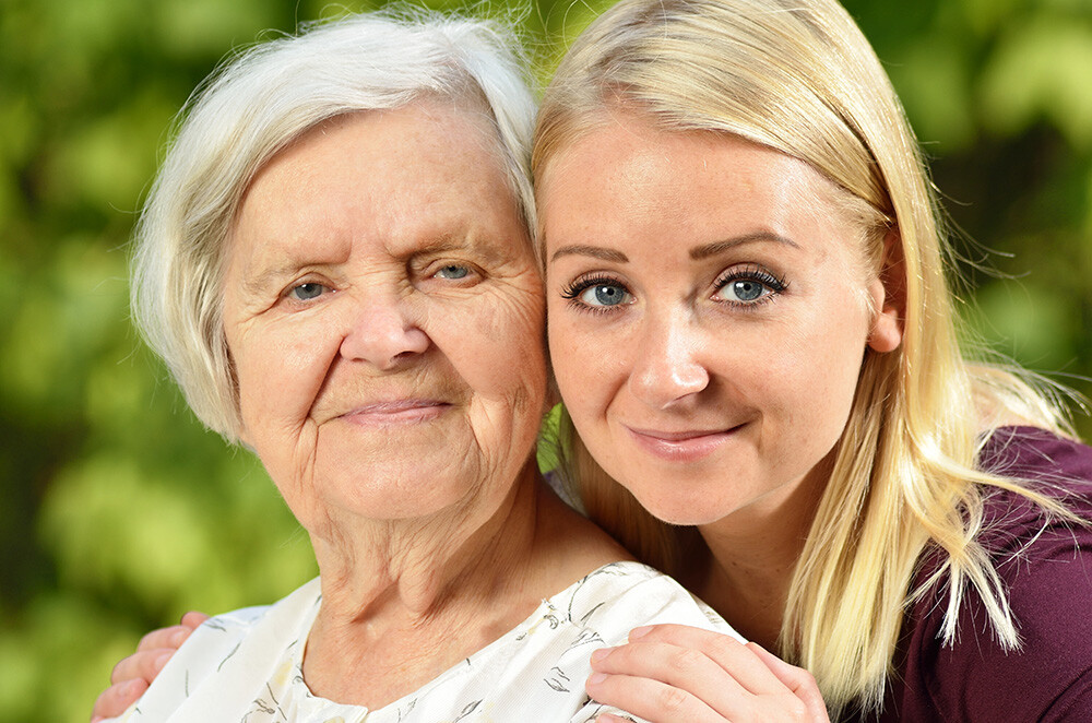 Elderly and a younger woman sitten outside.